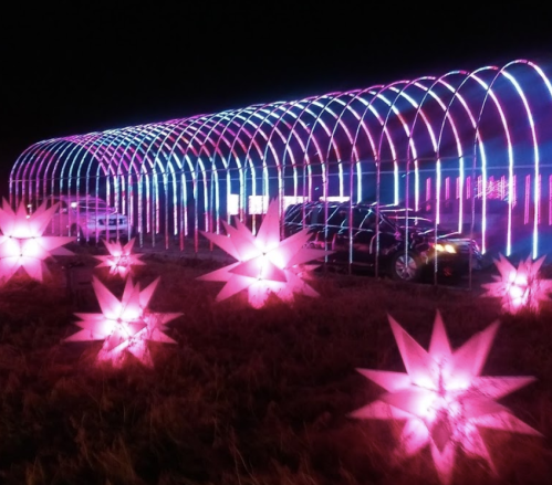 A brightly lit structure with pink and blue lights, surrounded by star-shaped light decorations in a dark setting.