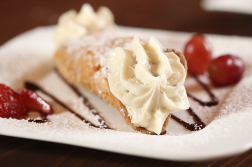 A delicious cannoli filled with cream, dusted with powdered sugar, and garnished with strawberries and chocolate sauce.