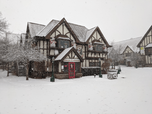 A charming Tudor-style building decorated for Christmas, surrounded by falling snow and a winter landscape.