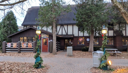 A charming, Tudor-style restaurant with festive decorations and outdoor seating, surrounded by trees and fallen leaves.