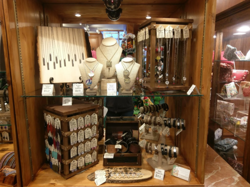 Display case filled with various jewelry items, including necklaces, bracelets, and earrings, on wooden shelves.