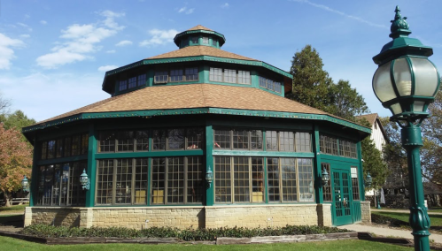A green octagonal gazebo with large windows, surrounded by trees and a decorative lamp post.