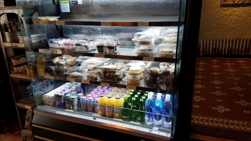 A display fridge filled with various desserts, snacks, and beverages, including juices and bottled water.