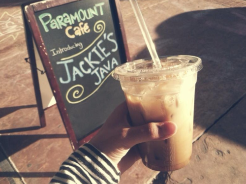 A hand holding an iced coffee in front of a sign for Paramount Café introducing Jackie's Java.