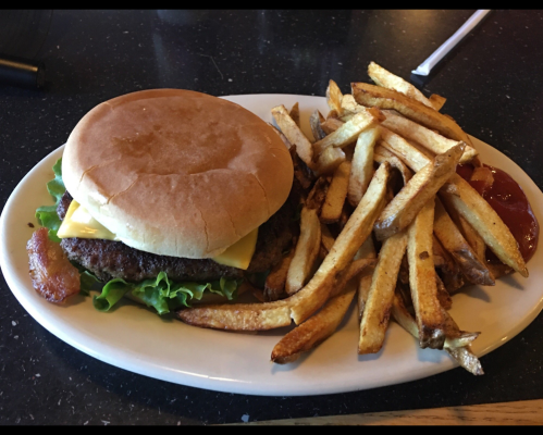 A plate with a cheeseburger topped with lettuce and a bun, accompanied by a side of golden fries and ketchup.