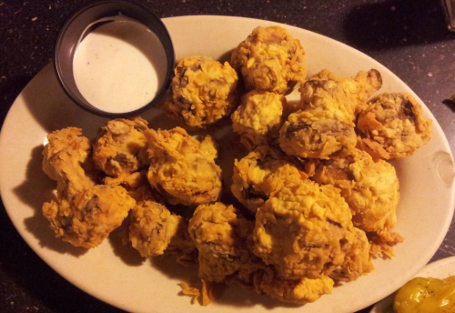 A plate of golden-brown fried mushrooms with a side of dipping sauce.