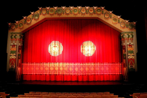 A vibrant red theater curtain with decorative patterns and two circular lights, set against an ornate stage backdrop.