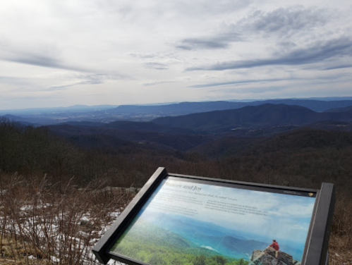 A scenic mountain view with a sign in the foreground, showcasing rolling hills and a cloudy sky.