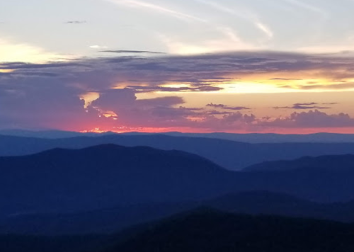 A vibrant sunset over layered mountains, with colorful clouds and a serene sky.
