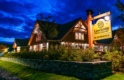 A cozy building at night with a sign reading "Lawson's Finest Liquids" and a well-lit entrance surrounded by greenery.