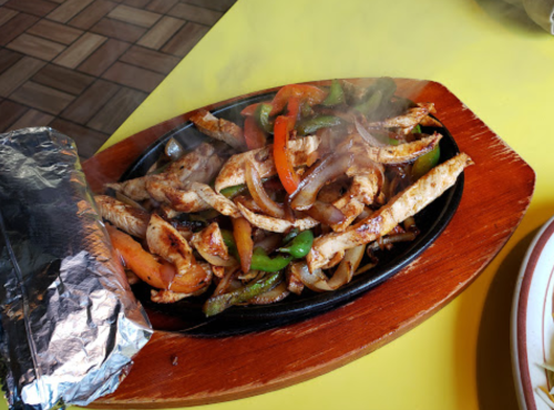 Sizzling fajitas with grilled chicken, bell peppers, and onions on a wooden platter, steam rising.
