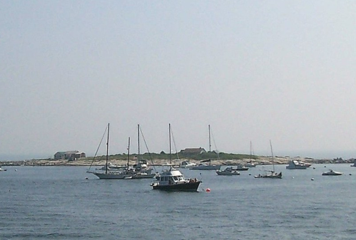 A serene coastal scene with several boats anchored near a small island under a clear sky.
