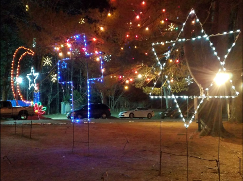 Colorful holiday lights in various shapes, including stars and a cross, illuminate a nighttime outdoor scene.