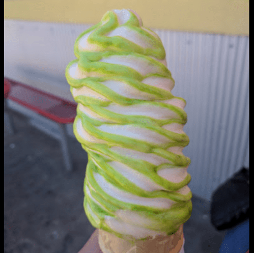 A swirl of green and white soft serve ice cream on a cone, held against a bright yellow background.