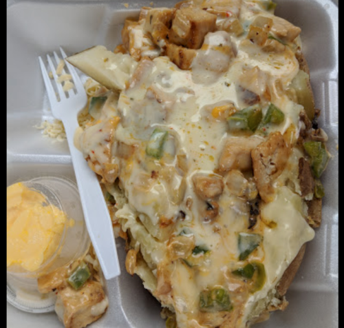 A loaded baked potato topped with chicken, green peppers, and melted cheese, served with a side of butter.