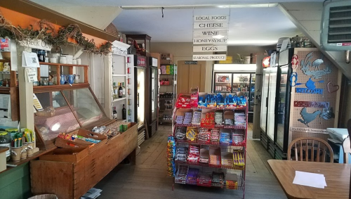 A cozy store interior featuring shelves of snacks, local foods, and a display of drinks and produce.