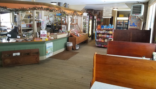 A cozy interior of a small store with wooden booths, a counter, and shelves stocked with snacks and drinks.