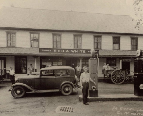 Historic black-and-white photo of a gas station with a vintage car and people in front of a store named "Chain Red & White."