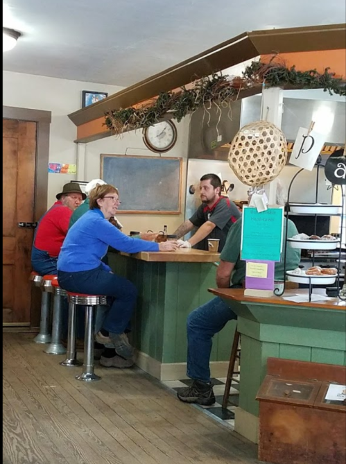 A cozy café scene with two customers chatting at the counter while a server prepares their order.
