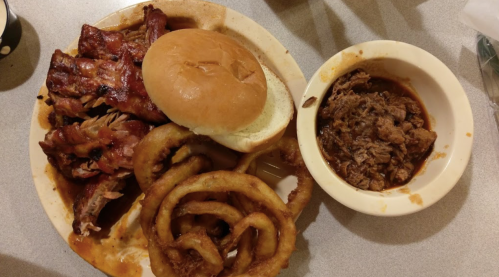 A plate of barbecue ribs, a bun, pulled pork, and onion rings on a table.