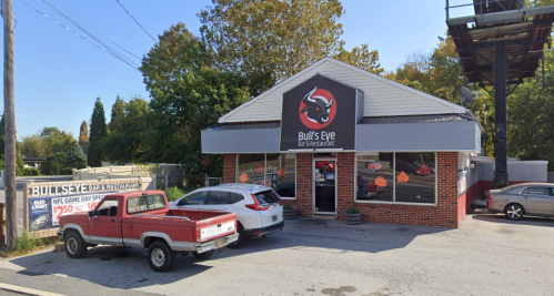 Exterior of Bull's Eye Bar & Restaurant, featuring a sign with a bull's eye logo and parked vehicles in front.