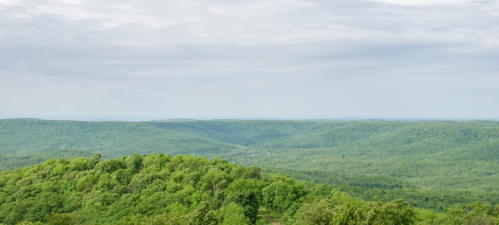 Lush green hills stretch under a cloudy sky, showcasing a serene landscape of rolling terrain.