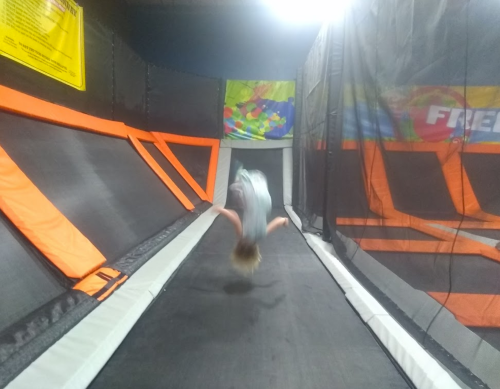 A child performs a backflip on a trampoline in a brightly colored indoor trampoline park.