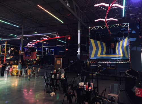 A vibrant indoor amusement center with neon lights, trampolines, and seating areas.