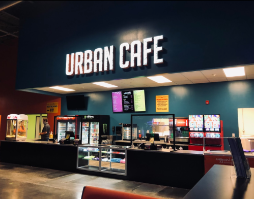 A brightly lit Urban Cafe with a menu board, vending machines, and a snack counter in a modern setting.