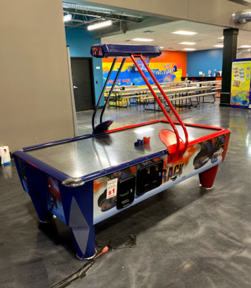 A blue and red air hockey table in a recreational space, with a dollar slot and no players.