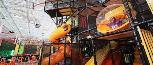 A colorful indoor playground with slides and climbing structures, featuring a smiling child in a clear bubble.