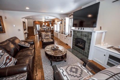 Cozy living room with leather sofas, a coffee table, and a large TV, leading to a kitchen area in a warm, inviting space.