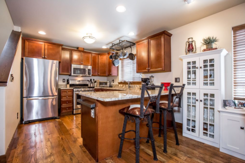 Modern kitchen with wooden cabinets, stainless steel appliances, and a central island with bar stools. Bright and inviting space.