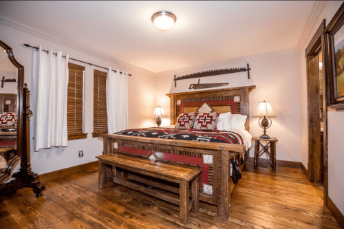 Cozy bedroom featuring a wooden bed, decorative blanket, and warm lighting with rustic decor and wooden flooring.