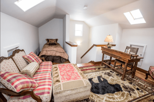 Cozy attic room with a bed, vintage sofa, desk, and skylights, featuring a patterned rug and warm lighting.