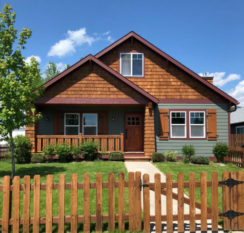 A charming two-story house with a wooden fence, green lawn, and blue sky in the background.