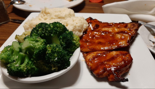 A plate with grilled chicken in sauce, steamed broccoli, and creamy mashed potatoes.