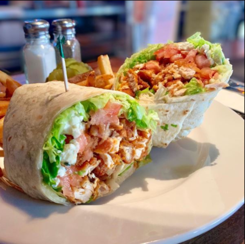 A close-up of a chicken wrap filled with lettuce and tomatoes, served with fries on a plate.
