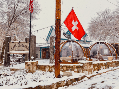 A snowy scene featuring a café with outdoor seating, a Swiss flag, and a sign reading "Café Gallery."