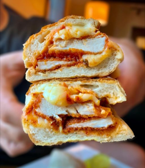 A close-up of a sandwich cut in half, revealing layers of chicken, cheese, and marinara sauce in a toasted bun.