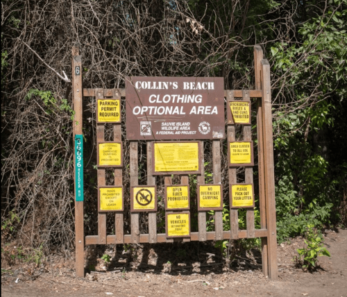 Sign at Collin's Beach indicating it's a clothing optional area with various rules and regulations posted.