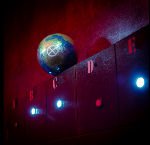 A colorful egg rests on a dark wall with letters A to E, illuminated by blue lights.