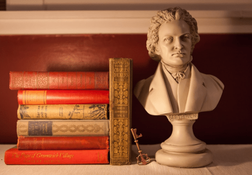 A bust of Beethoven beside a stack of vintage books with red and gold covers, and a decorative key on a table.