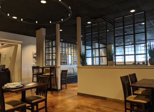 Interior of a modern restaurant featuring wooden tables, chairs, and a partition with plants, creating a cozy atmosphere.