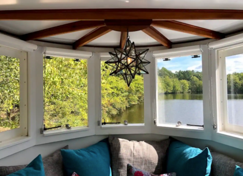 Cozy interior with a star-shaped light fixture, surrounded by windows overlooking a serene lake and lush greenery.