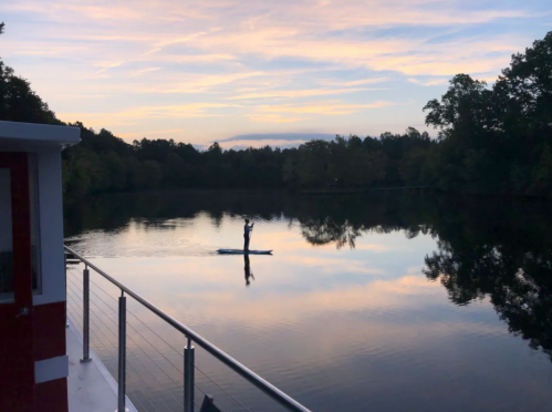 A person paddleboarding on a calm river at sunset, with trees reflecting in the water.