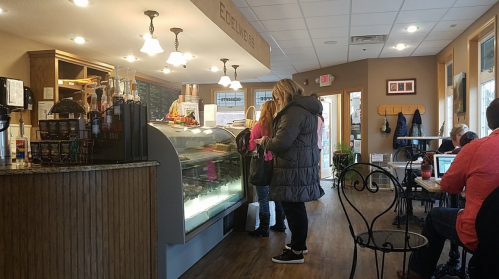 A cozy café interior with a display case, customers ordering, and others seated at tables working on laptops.