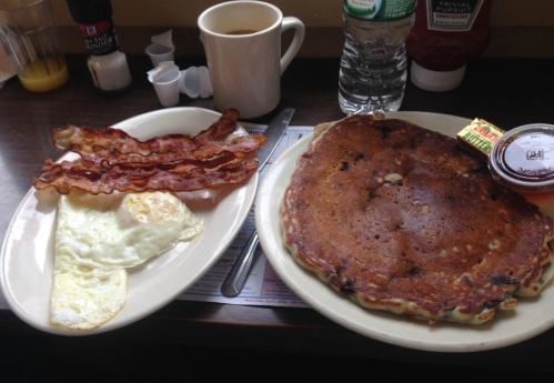 A plate with bacon, eggs, and a large pancake, alongside a cup of coffee and a bottle of water.