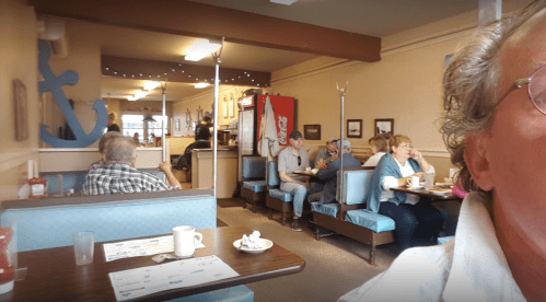 A cozy diner scene with patrons seated at tables, enjoying meals, and a glimpse of the interior decor.