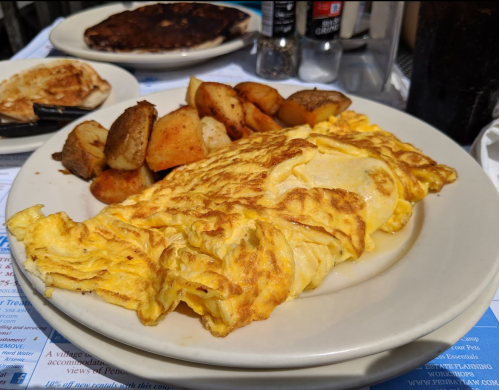 A plate of fluffy omelette with golden-brown roasted potatoes, served on a table with condiments in the background.